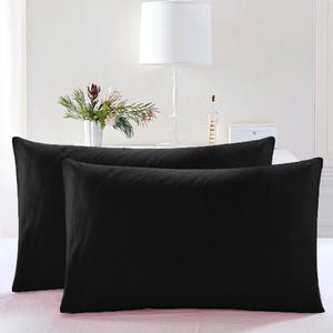May include: Two black pillowcases, one on top of the other, with a white lamp and a vase of flowers in the background.