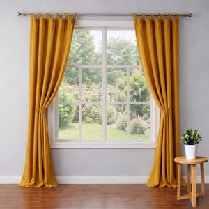 May include: Mustard yellow tab-top curtains framing a large window. The curtains are tied back, revealing a view of a lush green garden. A small wooden side table holds a potted plant, adding a touch of nature to the room.