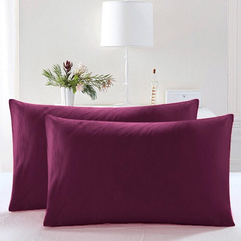 May include: Two purple pillowcases, one on top of the other, on a white bed. The pillowcases are made of a soft, smooth fabric.