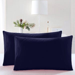 May include: Two navy blue pillowcases, one on top of the other, on a white bedspread.