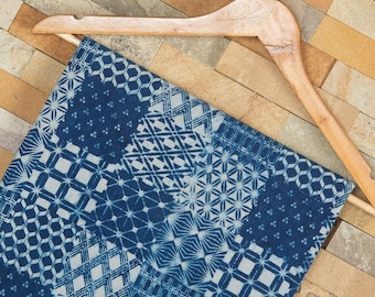 May include: A blue and white fabric with a patchwork design of geometric patterns. The fabric is hanging on a wooden hanger.