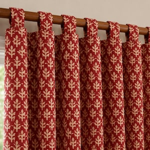 May include: A tab-top curtain panel featuring a deep red background with a repeating cream-colored botanical leaf pattern. The fabric hangs from a wooden curtain rod, creating vertical folds that showcase the consistent floral print design.