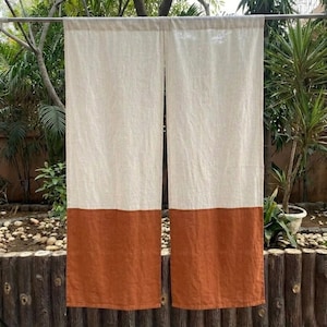 Könnte beinhalten: Zwei Leinen-Vorhänge mit zweifarbigem Design. Der obere Teil ist naturweiß, der untere Teil ist ein warmes, erdiges Orangebraun. Die Vorhänge hängen an einer Metallstange, mit Grün im Hintergrund.