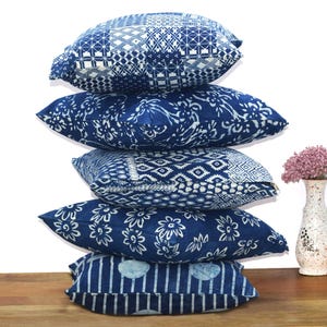 May include: A stack of five blue and white patterned throw pillows. The pillows are made of cotton and have a variety of geometric and floral designs.
