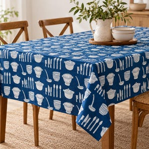 May include: A rectangular tablecloth featuring a deep blue background with a repeating white pattern of kitchenware, including pots, colanders, ladles, and various knives. The fabric covers a wooden table, displaying a consistent culinary motif.