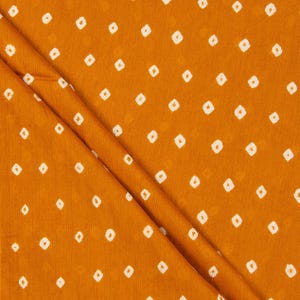 Puede incluir: Tela de color amarillo mostaza con un patrón repetitivo de pequeños rombos blancos. La tela está doblada, creando líneas diagonales. La textura parece suave y ligeramente texturizada. Ideal para textiles.