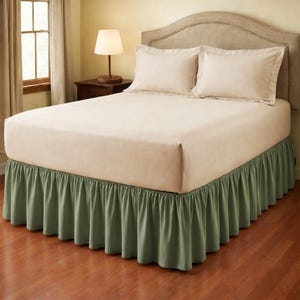 May include: A bed with a beige fitted sheet, two matching pillowcases, and a sage green bed skirt. A wooden nightstand with a lamp sits next to the bed. The headboard is upholstered in a neutral fabric.