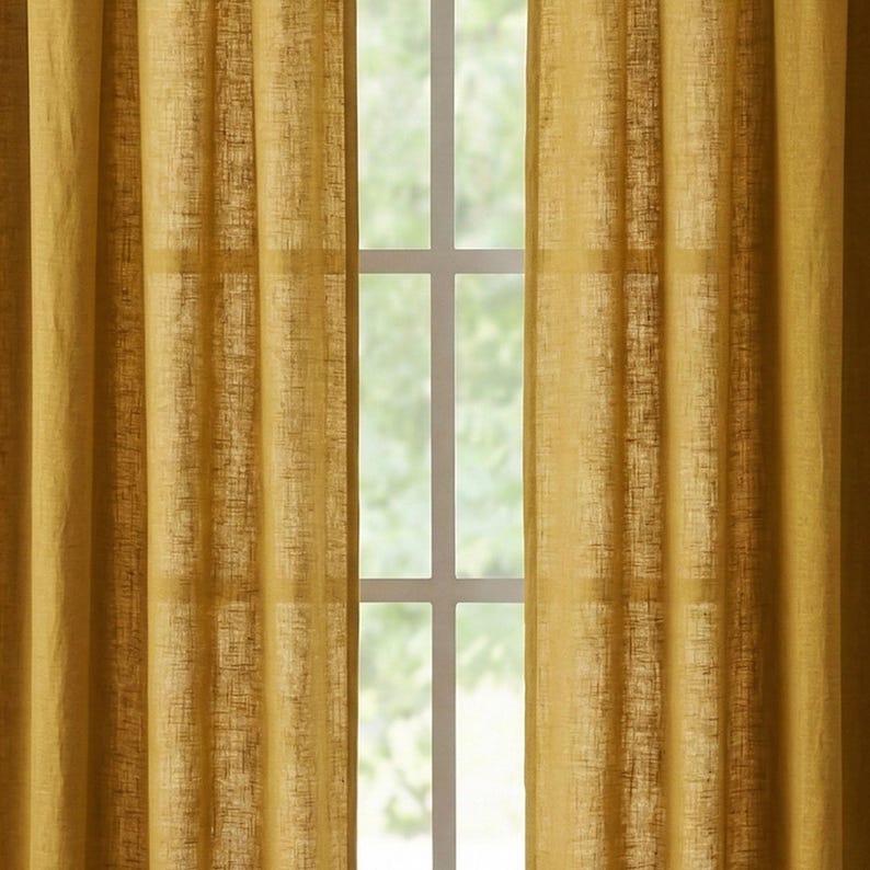 May include: Mustard yellow linen curtains hanging in front of a white window frame. The curtains have a textured appearance and are slightly translucent, allowing some light to pass through. The window is divided into multiple panes.