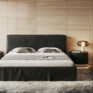 May include: A black upholstered bed frame with a tall, paneled headboard and a matching black bed skirt. The bed is dressed with white linens, a gray runner, and two patterned throw pillows. Two black cylindrical nightstands flank the bed.