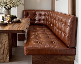 Könnte beinhalten: Eine braune Eckbank aus Leder mit tiefer Knopfheftung an Rückenlehne und Sitzfläche. Die Bank ruht auf einem Massivholzsockel und steht neben einem Esstisch aus Holz mit Baumkante, der eine natürliche Maserung und Textur aufweist.