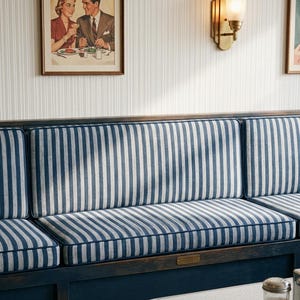 May include: A diner booth with blue and white striped cushions and a dark blue wooden base. The wall features framed vintage artwork and a brass sconce. The table has a white surface and chrome trim.