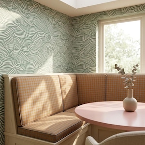May include: A cozy dining nook with a built-in bench featuring orange and yellow plaid cushions. The round table is painted pink, and the walls are adorned with a green and white wave pattern wallpaper. A vase with greenery sits on the table.