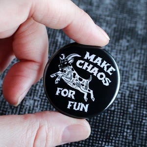 Könnte beinhalten: Ein schwarzer Knopf mit weißem Text und einer Ziegenillustration. Der Knopf lautet "MAKE CHAOS FOR FUN". Die Ziege ist weiß mit schwarzen Flecken. Der Knopf wird in einer Hand gehalten.