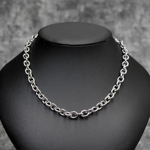May include: A silver-colored chain necklace with oval links is displayed on a black mannequin. The necklace is made of a shiny metal and has a classic, simple design. The background is a neutral gray.
