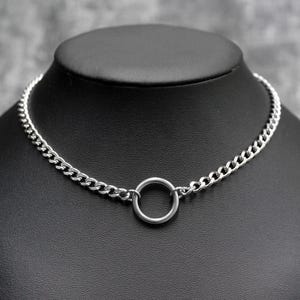 Puede incluir: Un collar gargantilla plateado con un diseño de cadena de eslabones y un colgante circular. El collar se exhibe en un maniquí negro. Los eslabones de la cadena están estrechamente unidos, creando una apariencia suave y continua. Mide unos 40 cm.