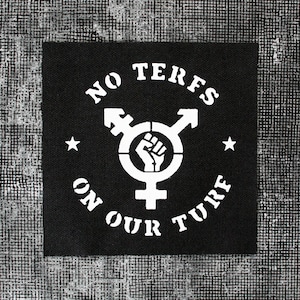 May include: Black and white patch with the text "NO TERFS ON OUR TURF" in a circle around a transgender symbol with a raised fist inside. Two white stars are on either side of the symbol.