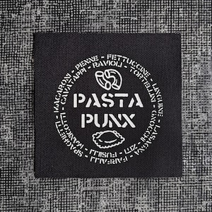 May include: A square black fabric patch featuring white embroidered text and graphics. The center displays the words PASTA PUNX with pasta shapes above and below. A circular border contains the names of various pasta types in white lettering.