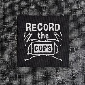 Peut inclure: Patch noir et blanc avec le texte "RECORD the COPS" et un dessin de mains tenant un téléphone.