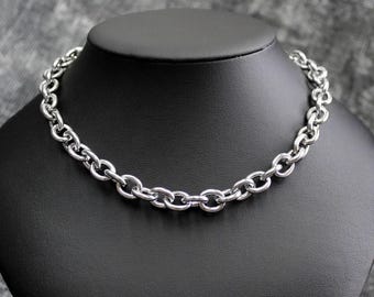 Puede incluir: Un collar de cadena plateada con eslabones ovalados se exhibe en un maniquí negro. El collar está hecho de un metal brillante y tiene un diseño simple pero elegante. La cadena es de estilo gargantilla.