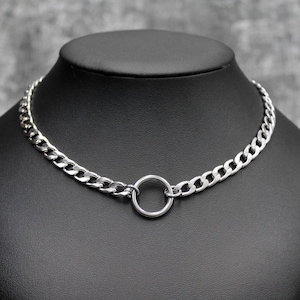 Puede incluir: Un collar de cadena plateada con un gran colgante circular. El collar se exhibe en un maniquí negro. Los eslabones de la cadena son gruesos y están conectados, creando un aspecto audaz e industrial.