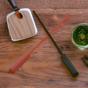 Puede incluir: Dos herramientas de limpieza con mangos negros y naranjas. Las herramientas están hechas de un material flexible y están cruzadas una sobre la otra. Las herramientas están sobre una superficie de madera.