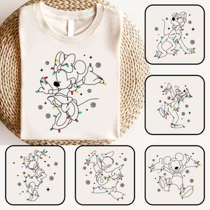 May include: Cream-colored t-shirt featuring a line drawing of Minnie Mouse adorned with Christmas lights and snowflakes. Additional square images showcase Mickey Mouse, Pluto, and Donald Duck in similar festive designs. The shirt is displayed on a woven basket.