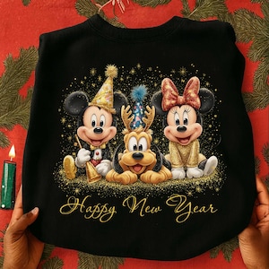 以下が含まれることがあります： ミッキーマウス、プルート、ミニーマウスがパーティー衣装を着た黒いスウェットシャツ。ミッキーはラッパを持ち、プルートはパーティーハットをかぶり、ミニーはリボンをしています。「Happy New Year」の文字は金色の筆記体で書かれています。金色の星と紙吹雪がキャラクターを囲んでいます。