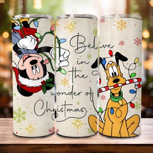 Peut inclure: Ensemble de trois gobelets isothermes en acier inoxydable avec des motifs de Noël. L'un présente Mickey Mouse avec des guirlandes lumineuses, un autre le texte "Believe in the wonder of Christmas", et le troisième Pluto avec un sucre d'orge.