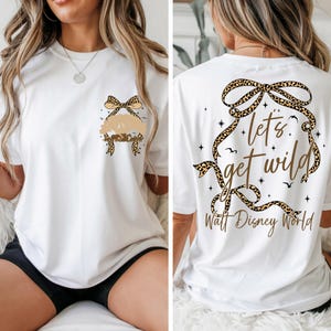 May include: White t-shirt with a leopard print bow and a tree graphic on the front. The back of the shirt features the text "Let's Get Wild" and "Walt Disney World" in gold lettering, surrounded by a leopard print ribbon.