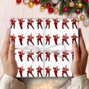 May include: A wrapped present with white paper patterned with a man in a red suit, Santa hat, and green tie. The gift is tied with white twine and held by two hands.