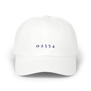 Peut inclure: Casquette de baseball blanche avec une visière incurvée. Le chapeau porte le numéro "02554" imprimé en bleu marine sur le devant. Le chapeau est fait d'une matière souple et a un style classique et décontracté.