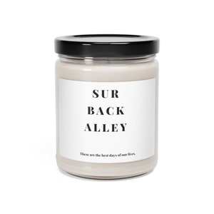 May include: A white candle jar with a black lid and a white label that reads "SUR BACK ALLEY" and "These are the best days of our lives."