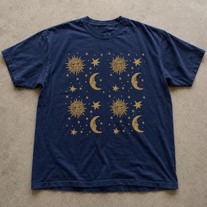 May include: A navy blue short-sleeve t-shirt featuring a repeating gold-colored print of suns, crescent moons with faces, and various stars arranged in a grid pattern across the center of the chest area of the garment.