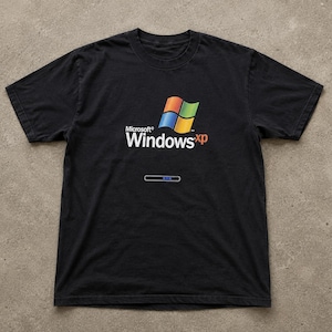 Könnte beinhalten: Ein schwarzes Kurzarm-T-Shirt mit dem Microsoft Windows XP-Logo in den typischen Farben Rot, Grün, Blau und Gelb. Unter dem Logo steht der Text Microsoft Windows xp, gefolgt von einer horizontalen Ladebalkengrafik mit blauen Segmenten.