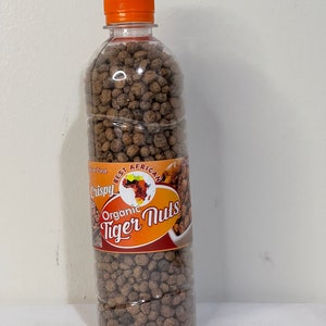 May include: A clear plastic bottle filled with brown tiger nuts, topped with an orange cap. The label reads "Crispy Organic Tiger Nuts" with an African continent graphic. The bottle is filled with small, round, textured nuts.