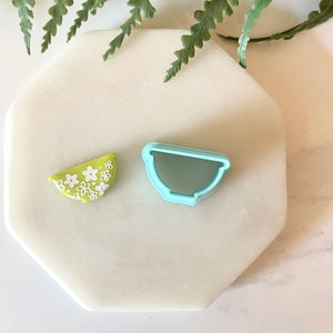 Pu&ograve; includere: Un tagliapasta a forma di ciotola verde e bianca e un tagliapasta a forma di ciotola in plastica blu chiaro su una superficie di marmo bianco.