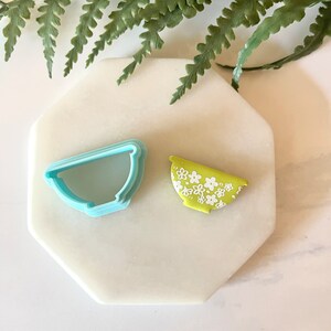 Pu&ograve; includere: Un tagliapasta in plastica blu a forma di ciotola e un biscotto verde e bianco decorato per assomigliare a una ciotola con un motivo floreale.
