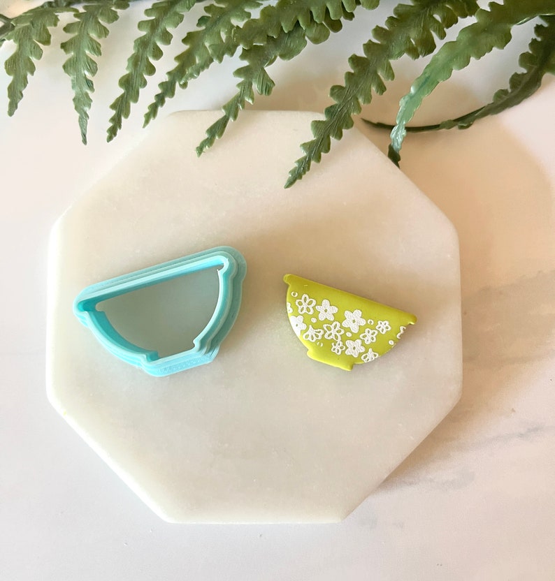 Pu&ograve; includere: Un tagliapasta in plastica blu a forma di ciotola e un biscotto verde e bianco decorato per assomigliare a una ciotola con un motivo floreale.