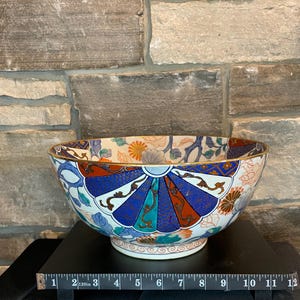 May include: A large, white ceramic bowl with a gold rim and intricate blue, red, and green floral and geometric designs. The bowl is approximately 9 inches in diameter.