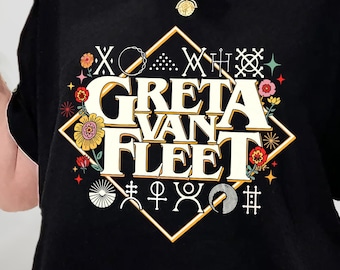 Op de afbeelding: Zwart T-shirt met een grafisch ontwerp met de tekst "Greta Van Fleet" in een gele lettertype, omringd door een ruitvorm. Het ontwerp bevat ook bloemen, sterren en andere symbolen.