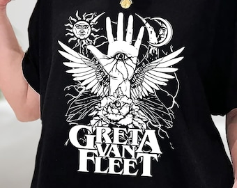 Op de afbeelding: Zwart T-shirt met een witte afbeelding van een hand met een oog, vleugels en de tekst "Greta Van Fleet".