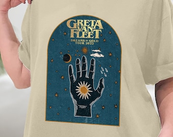 Op de afbeelding: Een beige T-shirt met een vintage-stijl grafische afbeelding van een hand die naar een zon en maan reikt. De afbeelding bevat de tekst "Greta Van Fleet" en "Dreams in Gold Tour 2022".
