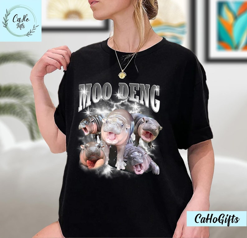 K&ouml;nnte beinhalten: Schwarzes T-Shirt mit einem Motiv von f&uuml;nf Baby-Fluss Pferden mit dem Text "Moo Deng" in silbernen Glitzerbuchstaben.
