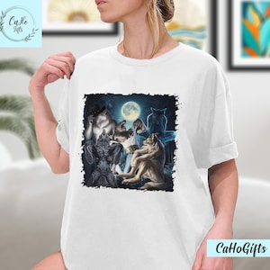 May include: A white t-shirt with a graphic print of a group of wolves howling at the moon. The wolves are depicted in a dark, shadowy setting with a full moon in the background.