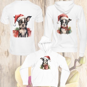 May include: Three white shirts with a Christmas-themed design featuring a black and white Boston Terrier puppy wearing a Santa hat and holding a red gift box. The shirts are available in a t-shirt and hoodie style.