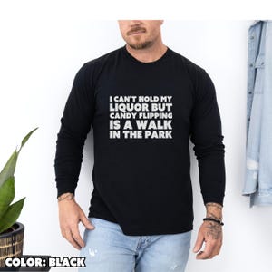 May include: Black long-sleeve shirt with the text "I CAN'T HOLD MY LIQUOR BUT CANDY FLIPPING IS A WALK IN THE PARK" in white. The shirt is a solid black color and is made of a soft material. The shirt is a casual style.