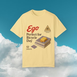 Könnte beinhalten: Ein gelbes T-Shirt mit einem Grafikdesign im Vintage-Stil. Die Grafik zeigt den Text "Ego Perfect for Bicycle Day" und einen Stapel gebutterter Waffeln. Der Text "PermaDosed Foods" ist ebenfalls im Design enthalten.