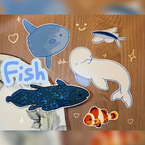 May include: A set of colorful fish stickers with the word "Fish" in blue letters. The stickers feature a blue fish, a white fish, a yellow and blue fish, a blue and black fish, and an orange and white fish.