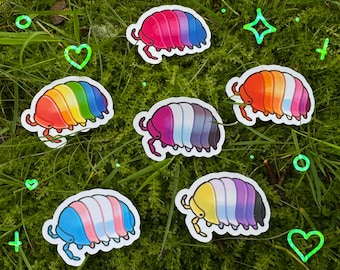 May include: Six colorful pill bug stickers with different pride flag designs. The stickers are on a green background of grass.