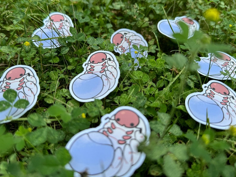 May include: A set of seven stickers featuring a cartoon pill bug with a light blue shell and pink body. The stickers are on a green grassy background.